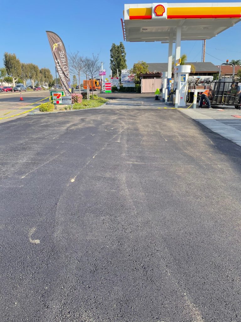 The image shows a newly paved asphalt parking lot in front of a Shell gas station.