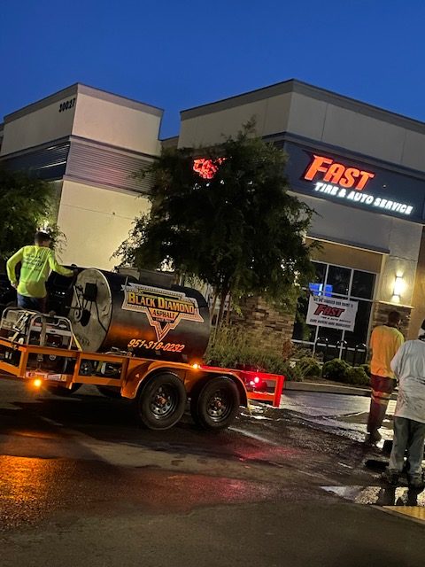 The image shows an asphalt paving crew working in front of a building